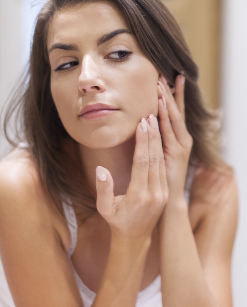 Brunette woman checking her skin in the mirror